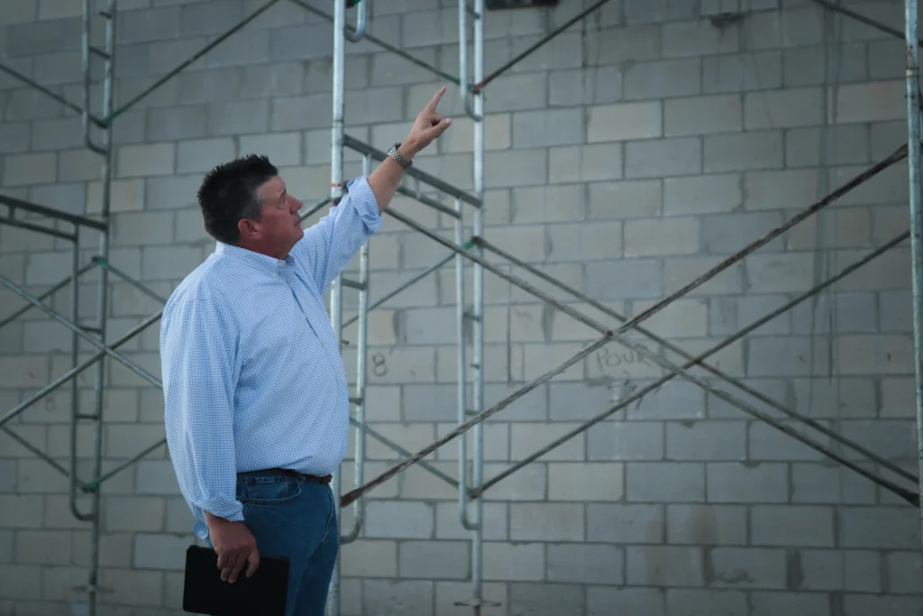 Mike Miller pointing at a concrete block construction wall, providing technical guidance for custom home builders in Florida.